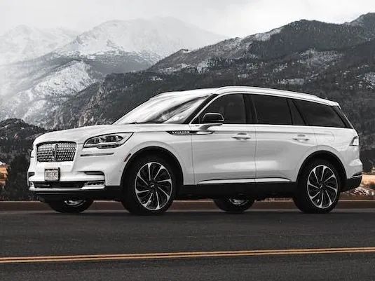 White SUV driving on a wet road with snowy mountains in the background