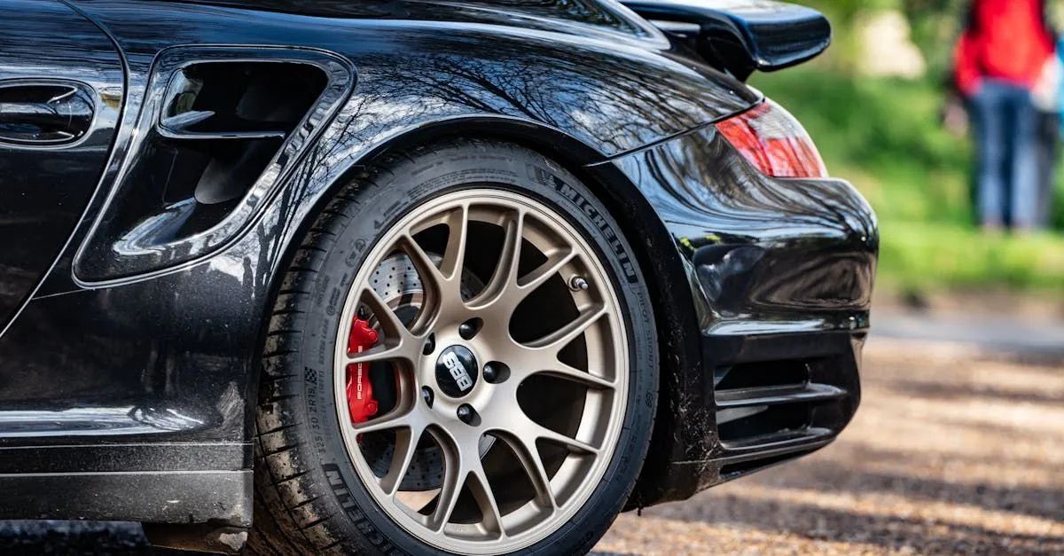 Close-up of a black sports car’s rear wheel with bronze rim and red brake caliper on a gravel road.