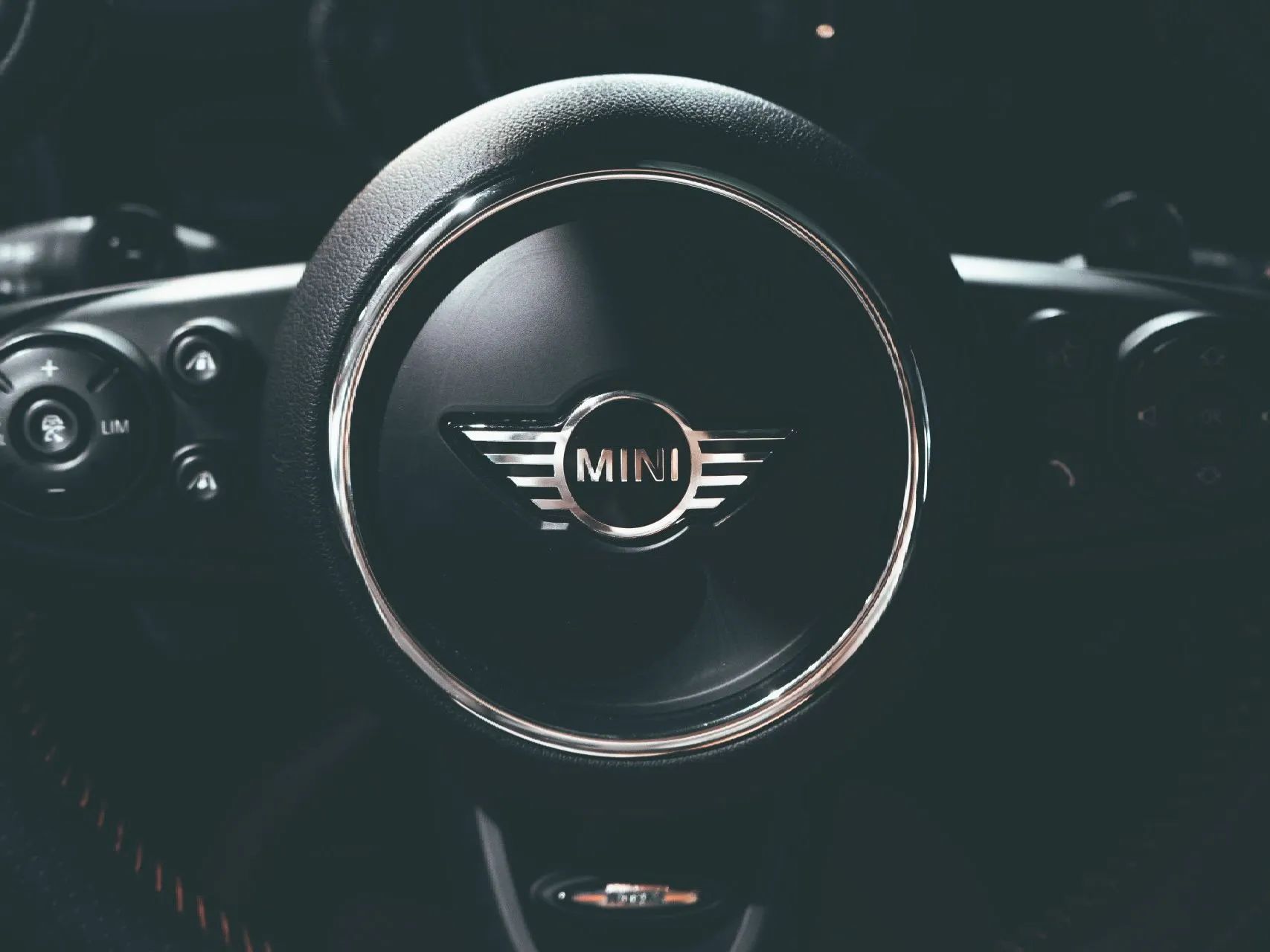 Close-up of a MINI car steering wheel with chrome logo and dark dashboard behind it