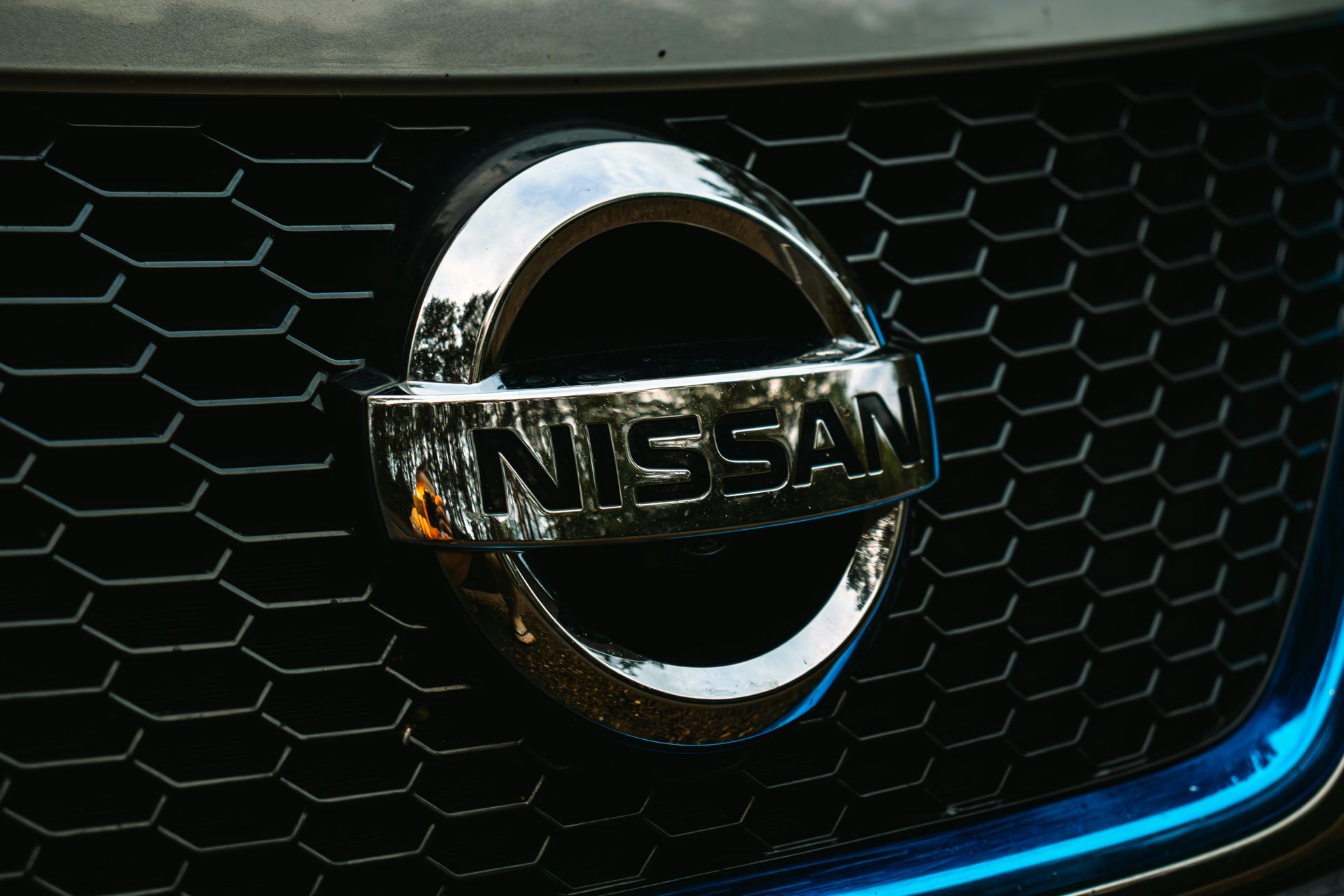 Close-up of a Nissan grille emblem with chrome logo on a black honeycomb front grille