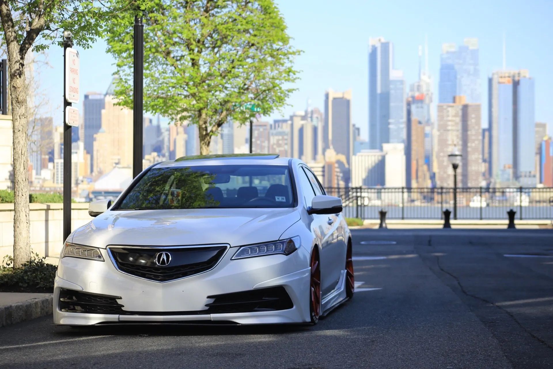 White Acura sedan parked by a waterfront with a city skyline in the background