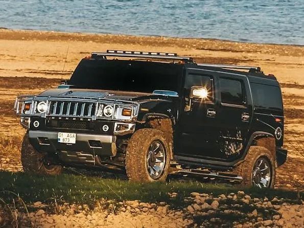 Black SUV parked on a rocky beach with ocean in the background