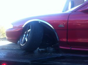 Red car with black wheels parked low on a wet street in bright sunlight