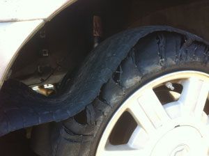 Damaged car tire with a large bulge and tear, close-up near the wheel well