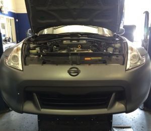 Front view of a black Nissan with hood open in a garage, exposing the engine compartment.