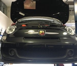 Black Abarth car with hood open in a garage, front view