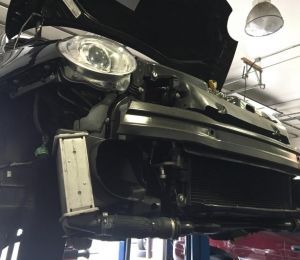 Front view of a black car raised on a lift in an auto repair garage, hood open.