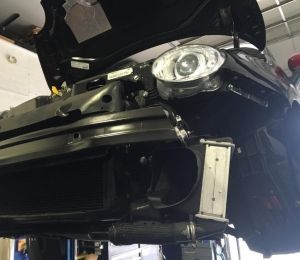 Black car front end with headlight and grille, viewed from below in a garage-like setting
