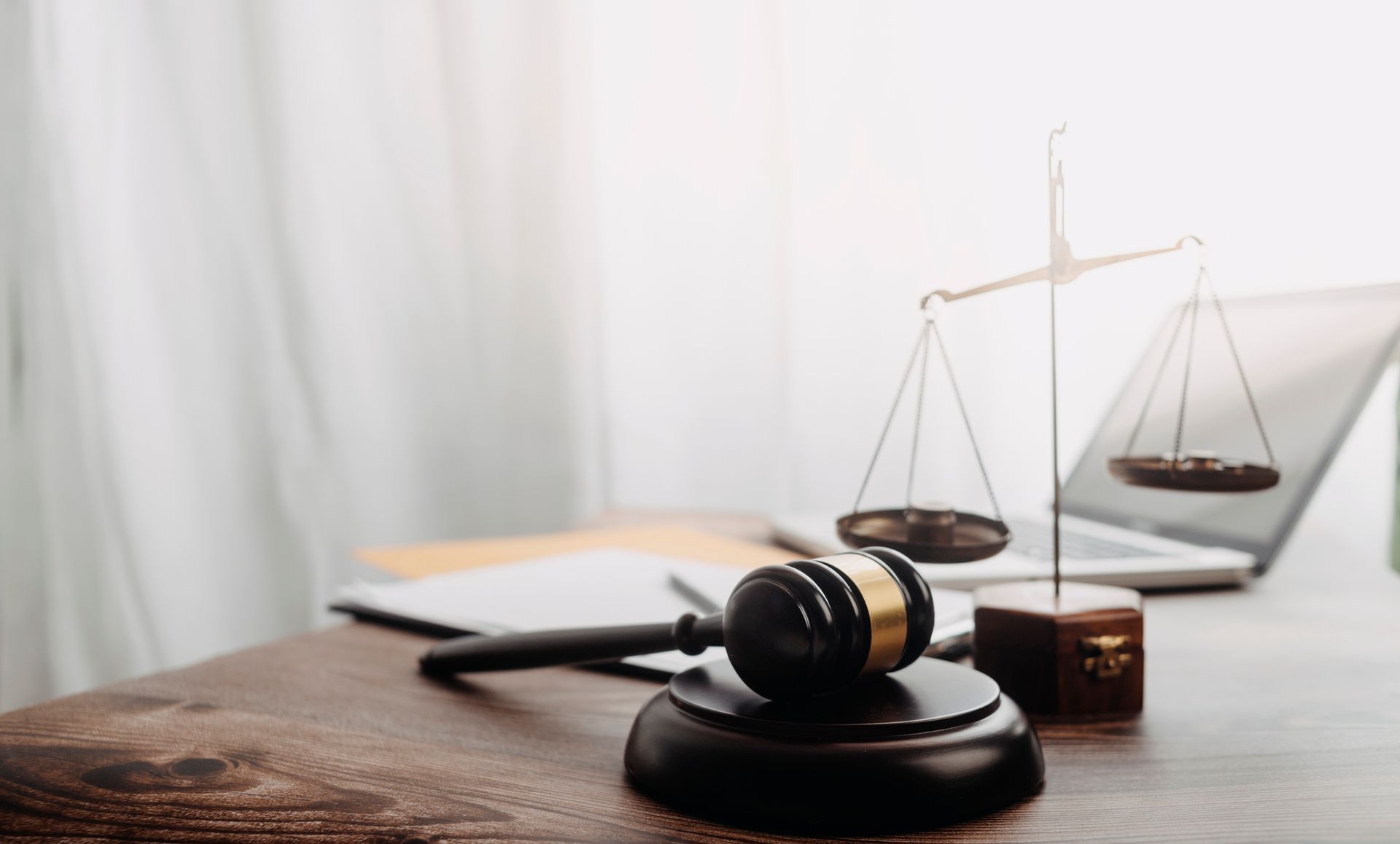 Gavel and scales of justice on a desk, near a laptop and a window.