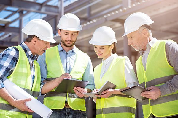 Four construction workers in hard hats and safety vests reviewing plans on a job site