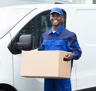Smiling delivery worker in blue uniform holding a cardboard box beside a white van