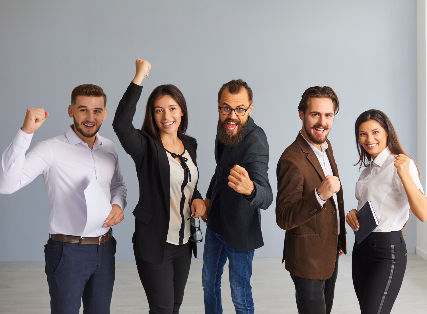 A diverse group of businesspeople celebrating with raised fists in a bright office.