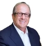 Smiling man in glasses and navy blazer against a white background