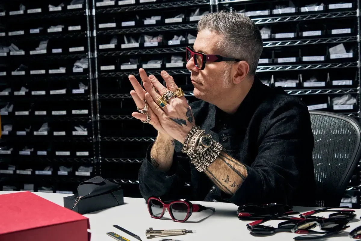 Person with glasses seated at a desk, holding hands together in front of a wall of small drawers.
