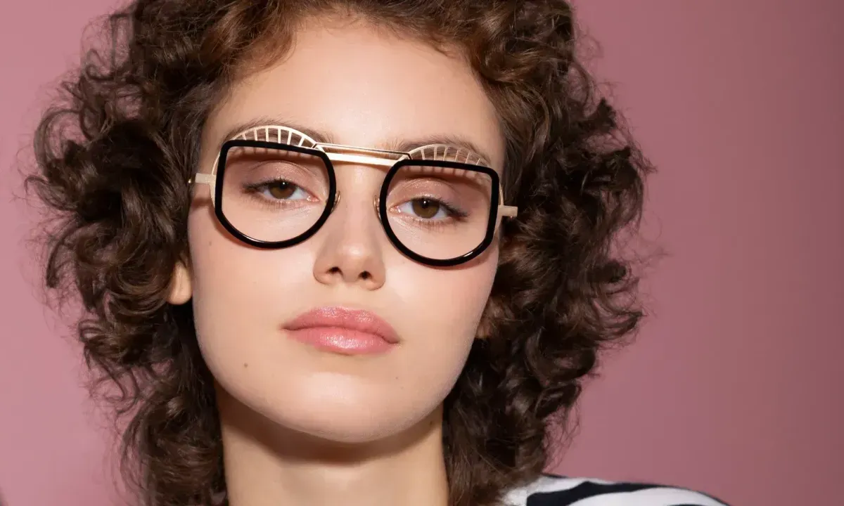 Person wearing oversized black glasses against a pink background