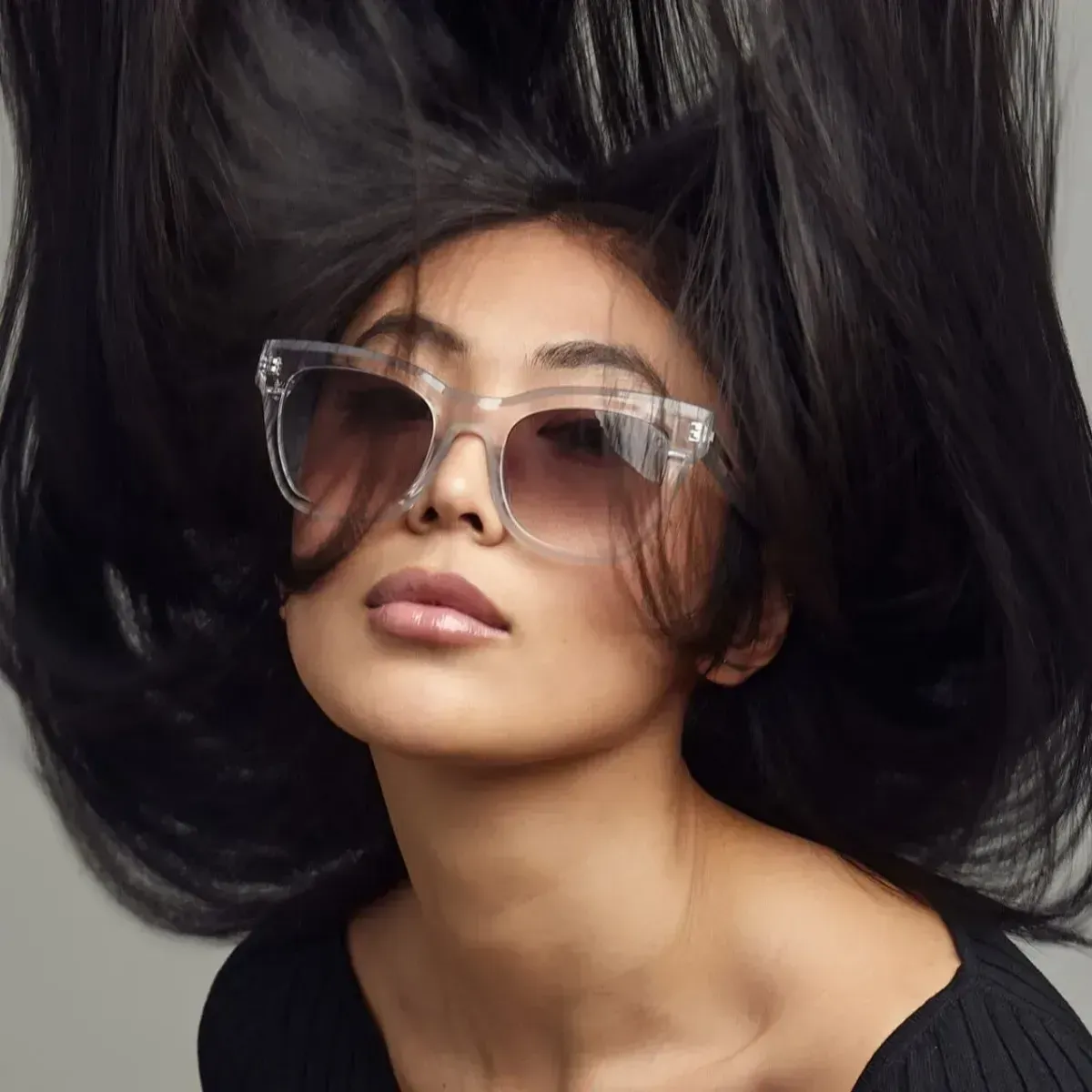 Woman with oversized clear glasses and voluminous black hair on a dark background