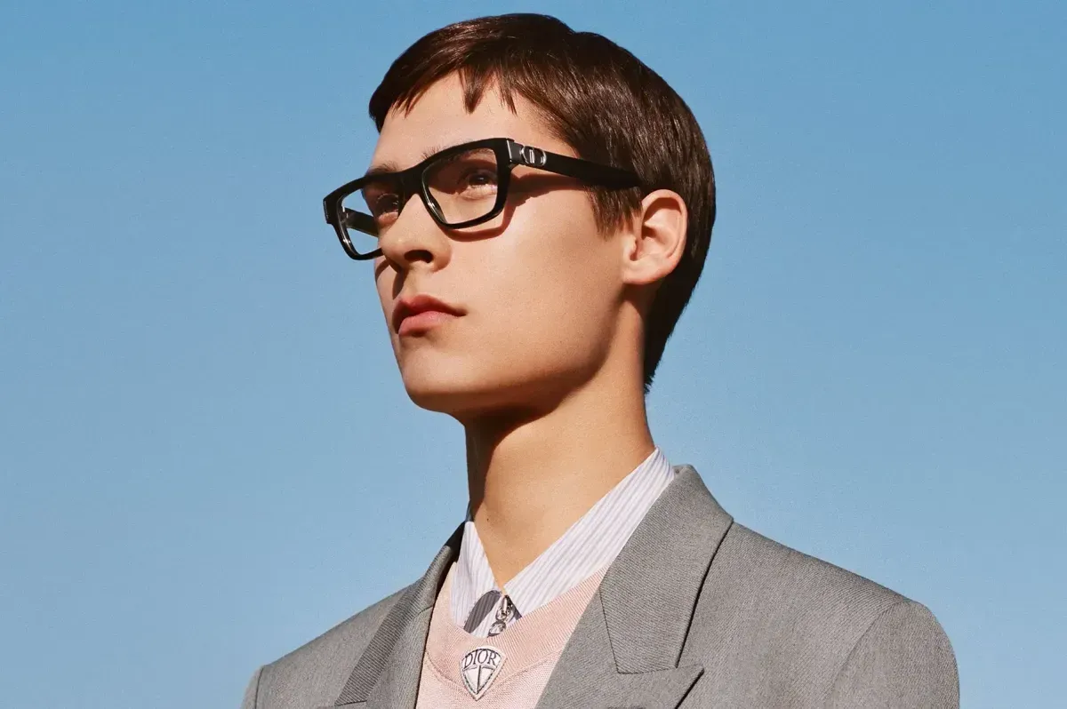 Person in glasses and a gray suit against a clear blue sky, looking upward.