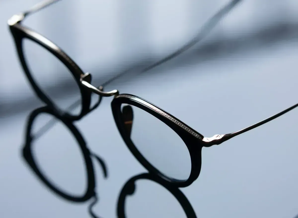 Black eyeglasses with thin frames resting on a reflective surface