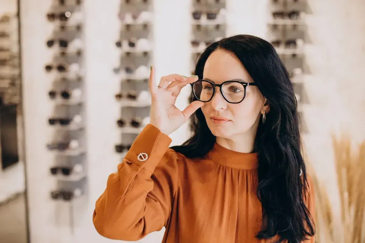 Person adjusting glasses in a warmly lit room with shelves in the background