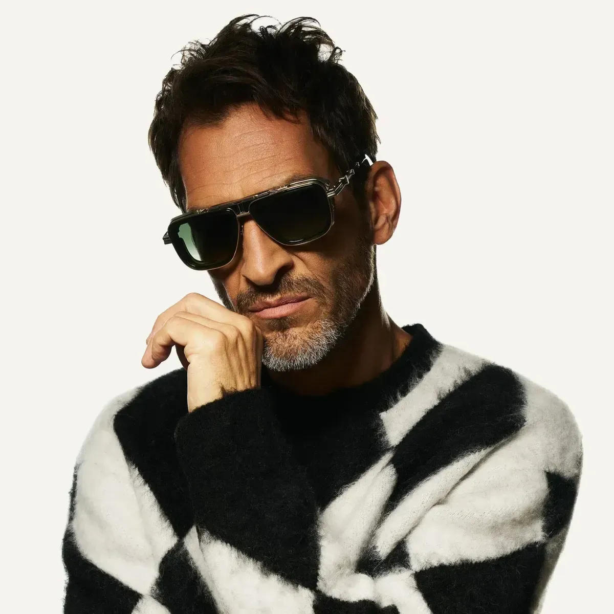 Man wearing sunglasses and a black-and-white patterned sweater, posing against a plain white background