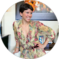 Woman in a floral dress posing indoors with hands on hips, smiling beside framed wall art