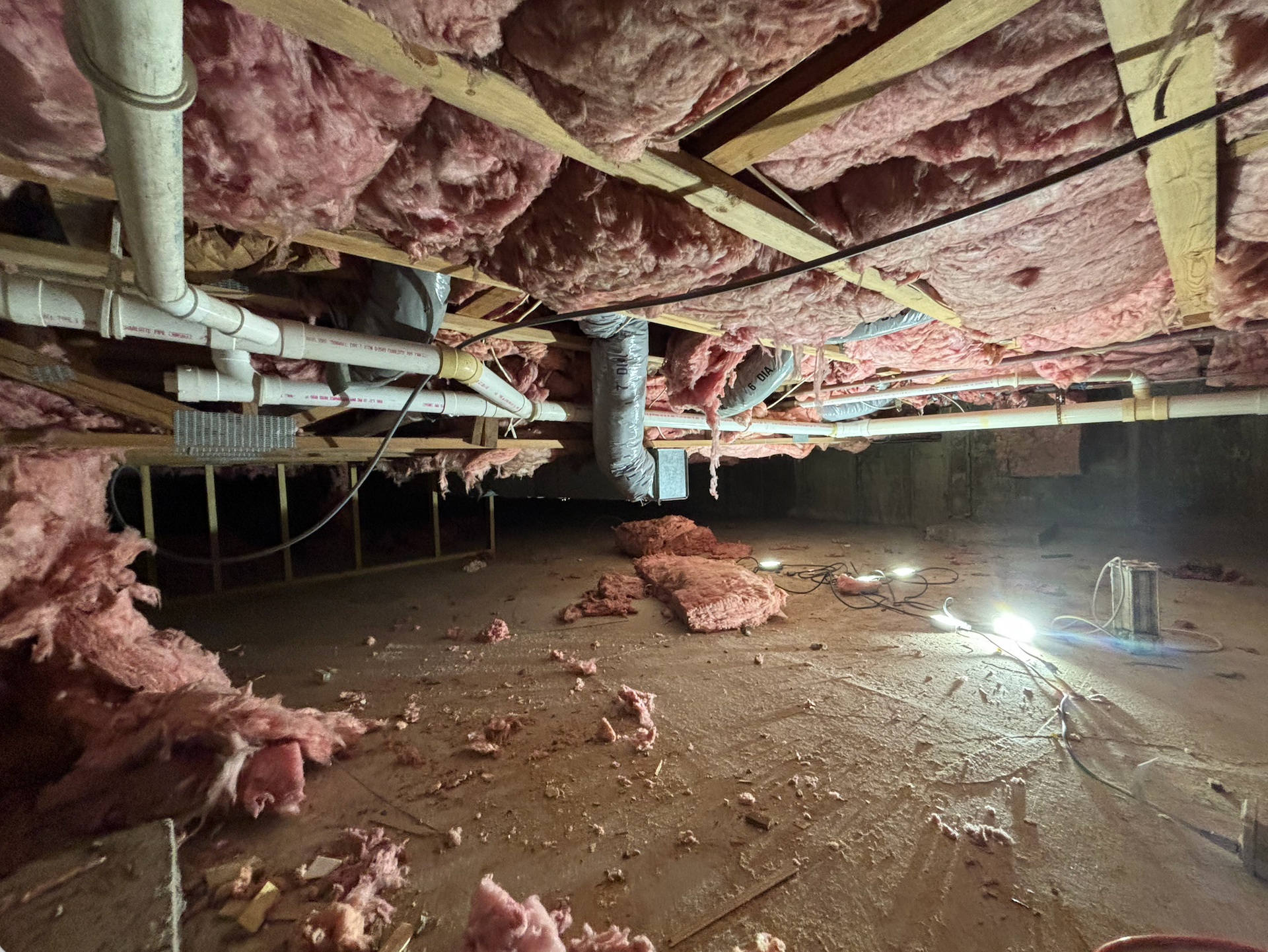 Unfinished basement crawl space with exposed pipes, insulation, and bare concrete