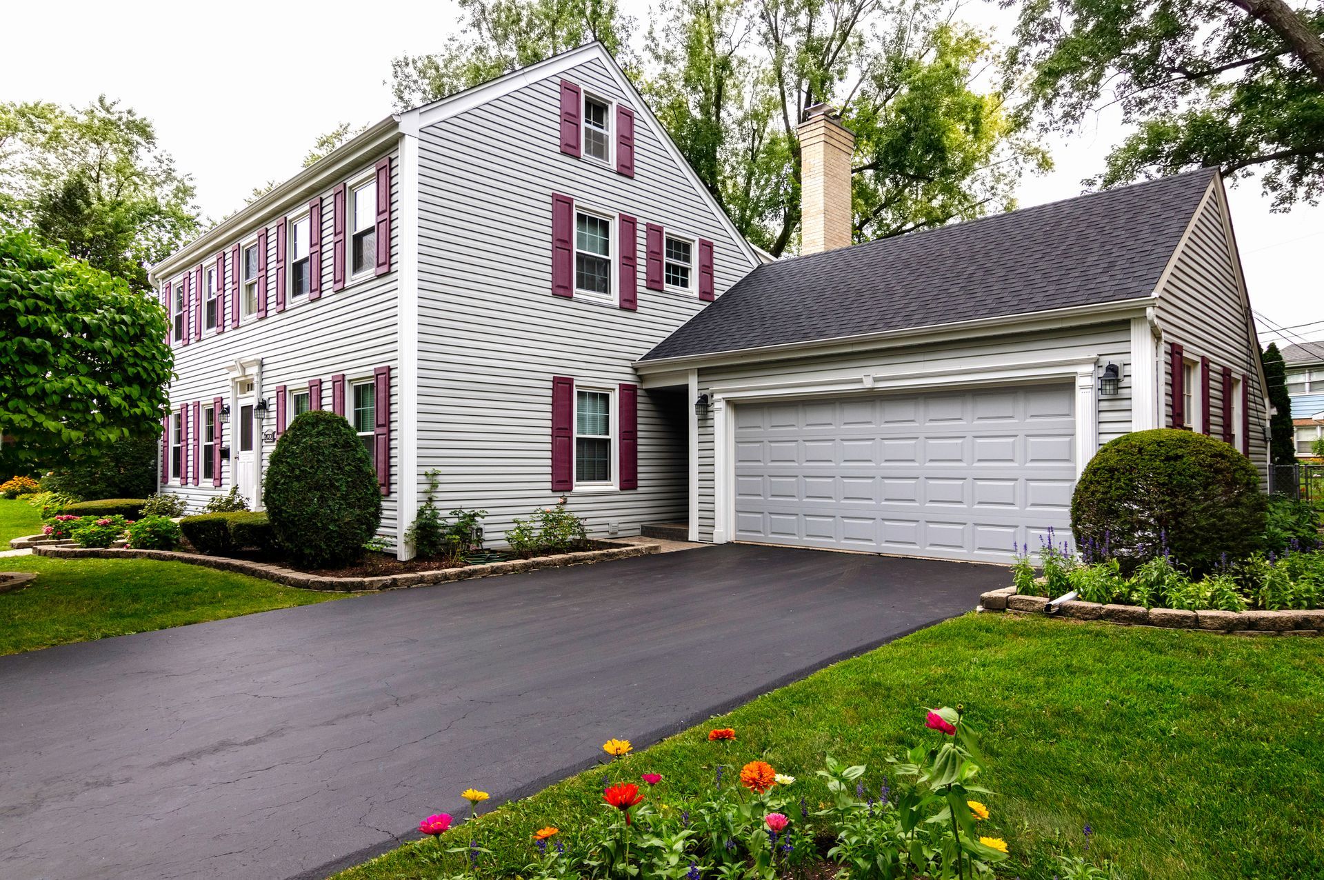 Two-story house with gray siding, red shutters, and an attached garage; driveway and landscaping.