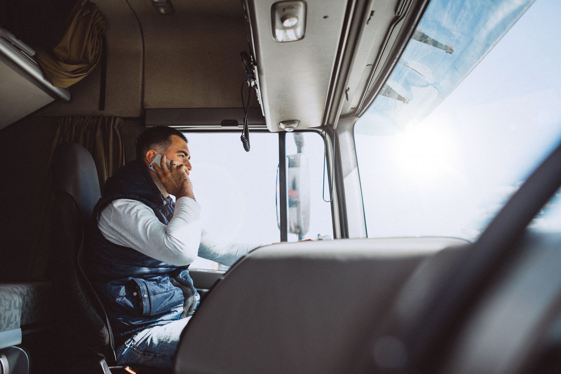 Man in truck cab talking on phone, sunlight streaming through the windshield.