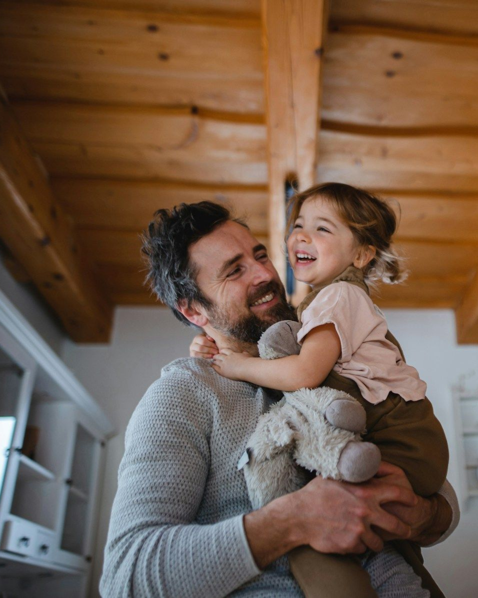 Man holding and smiling at a laughing child; wooden ceiling and beams.