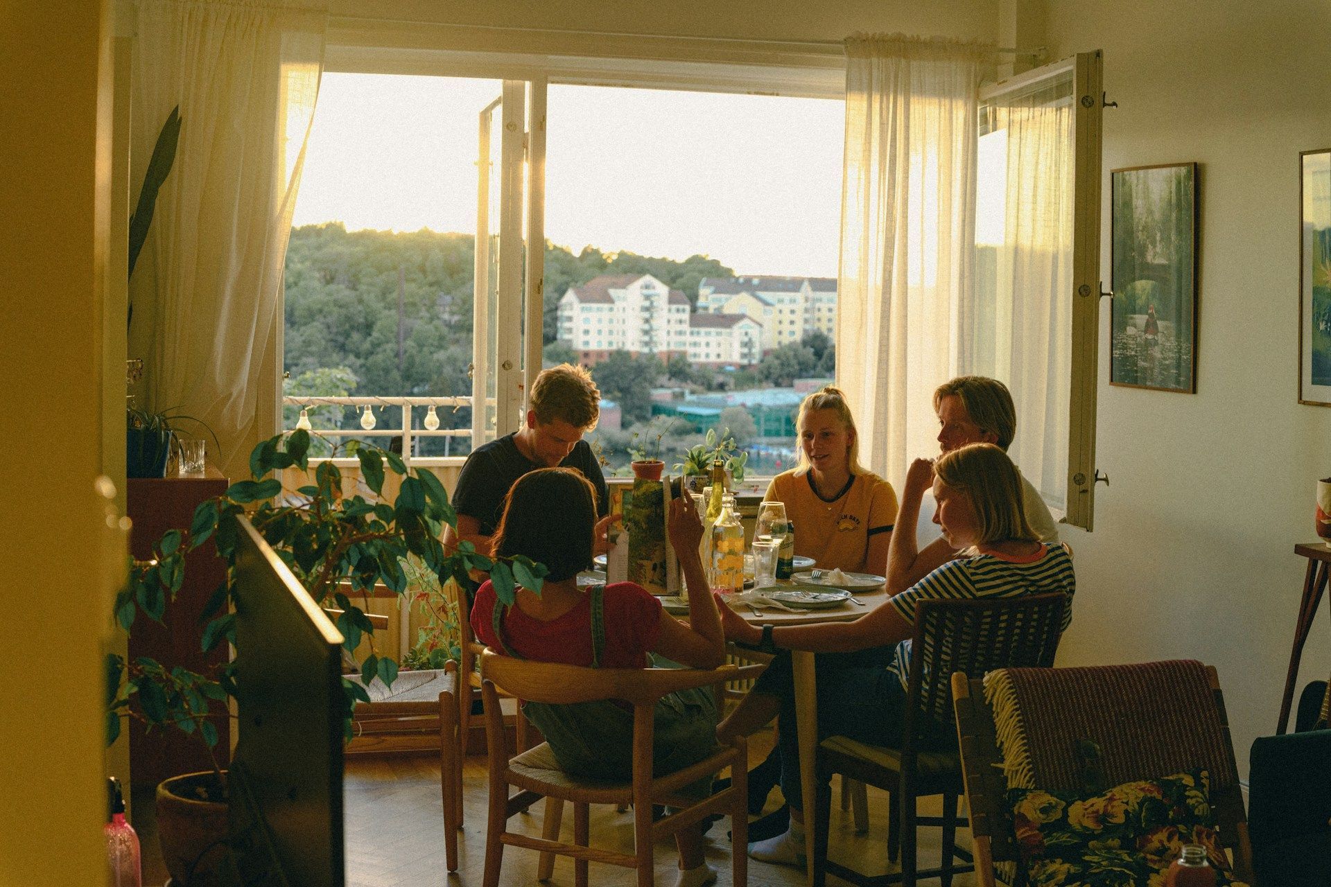 Five people at a table, looking out at a view from an apartment. Sunlight streams in.