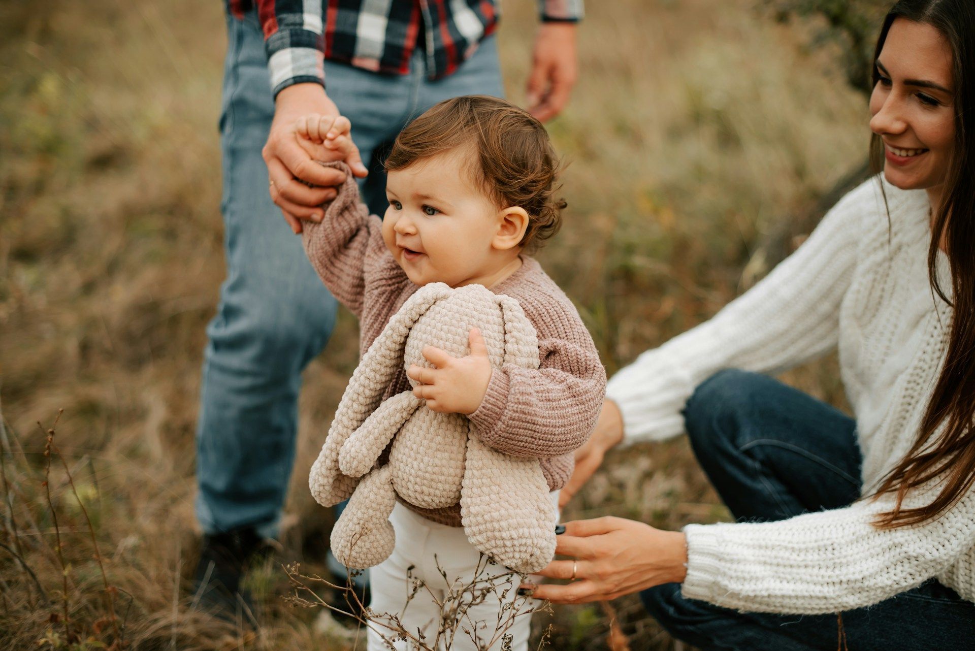 Family in outdoor setting with toddler holding a stuffed bunny, smiling.