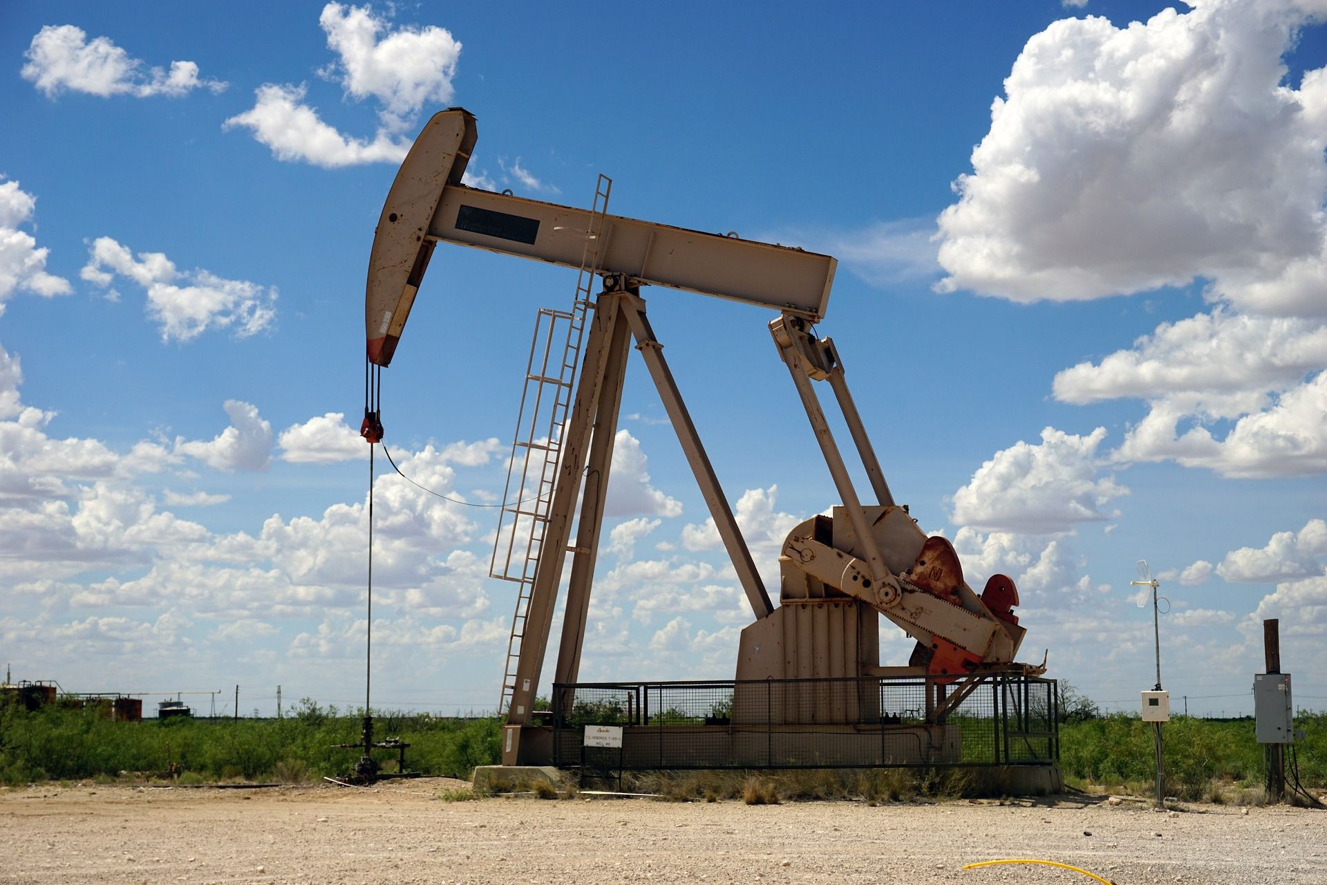 Oil pump jack in an open field, sky with clouds overhead.