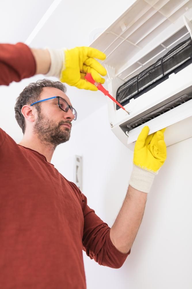 A Man Is Fixing An Air Conditioner With A Screwdriver — North West Heating, Cooling and Refrigeration in Taminda, NSW