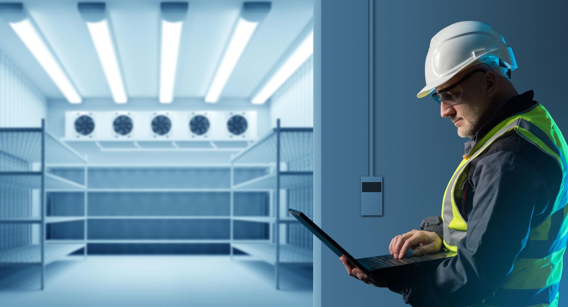 A Man In A Hard Hat Is Using A Laptop Computer In A Cool Room — North West Heating, Cooling and Refrigeration in Narrabri, NSW