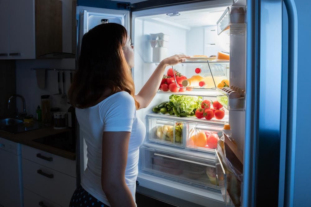 A Woman Looking For Food Inside A Refrigerator At Night North West Heating, Cooling and Refrigeration in Taminda, NSW