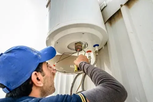 A Man Is Fixing A Water Heater On The Side Of A Building— North West Heating, Cooling and Refrigeration in Taminda, NSW