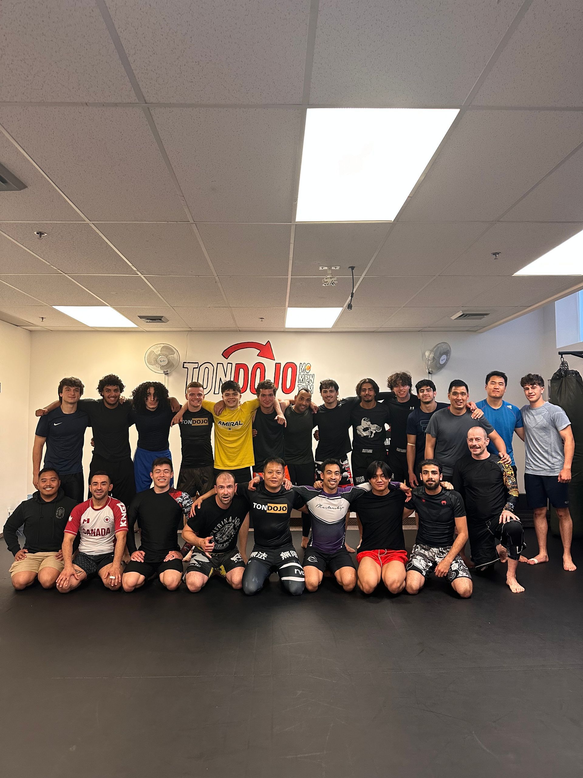 Groupe de personnes, probablement un cours d'arts martiaux, posant pour une photo dans une salle de sport.