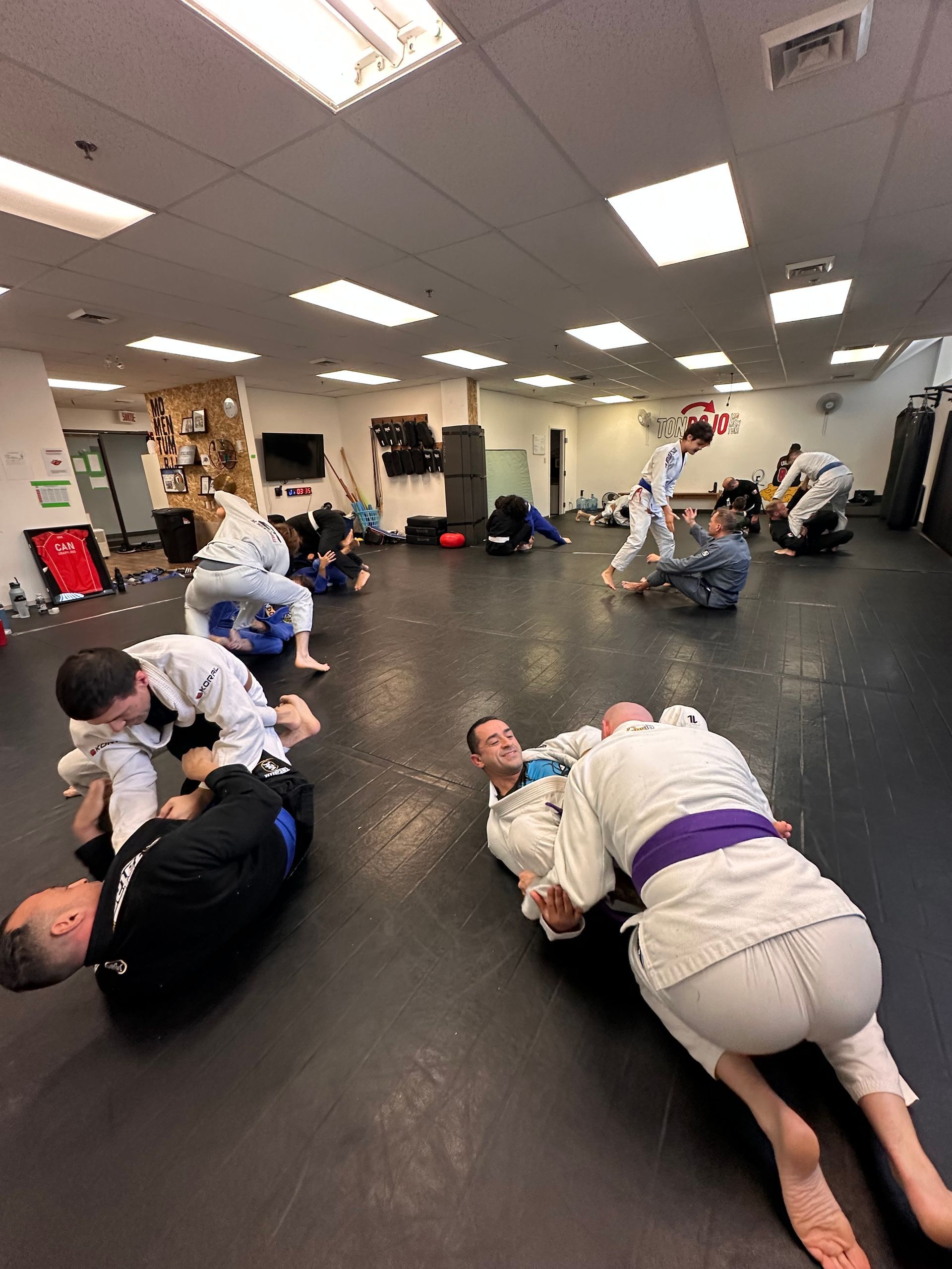 Des participants à un cours d'arts martiaux sur un tapis noir. Les élèves s'entraînent au grappin dans différentes positions.