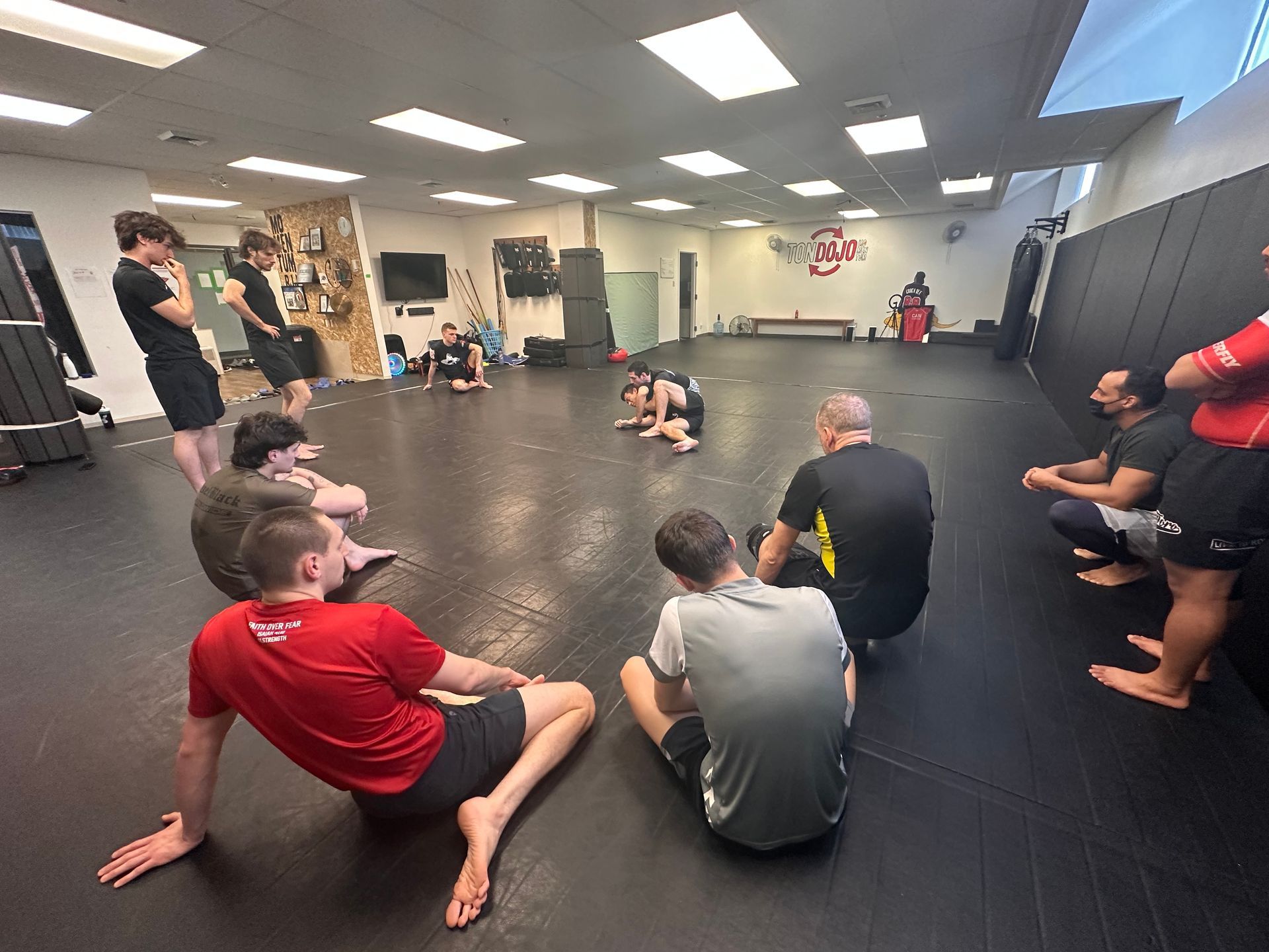 Des personnes dans un cours d'arts martiaux assis en cercle sur un tapis, observant une démonstration.