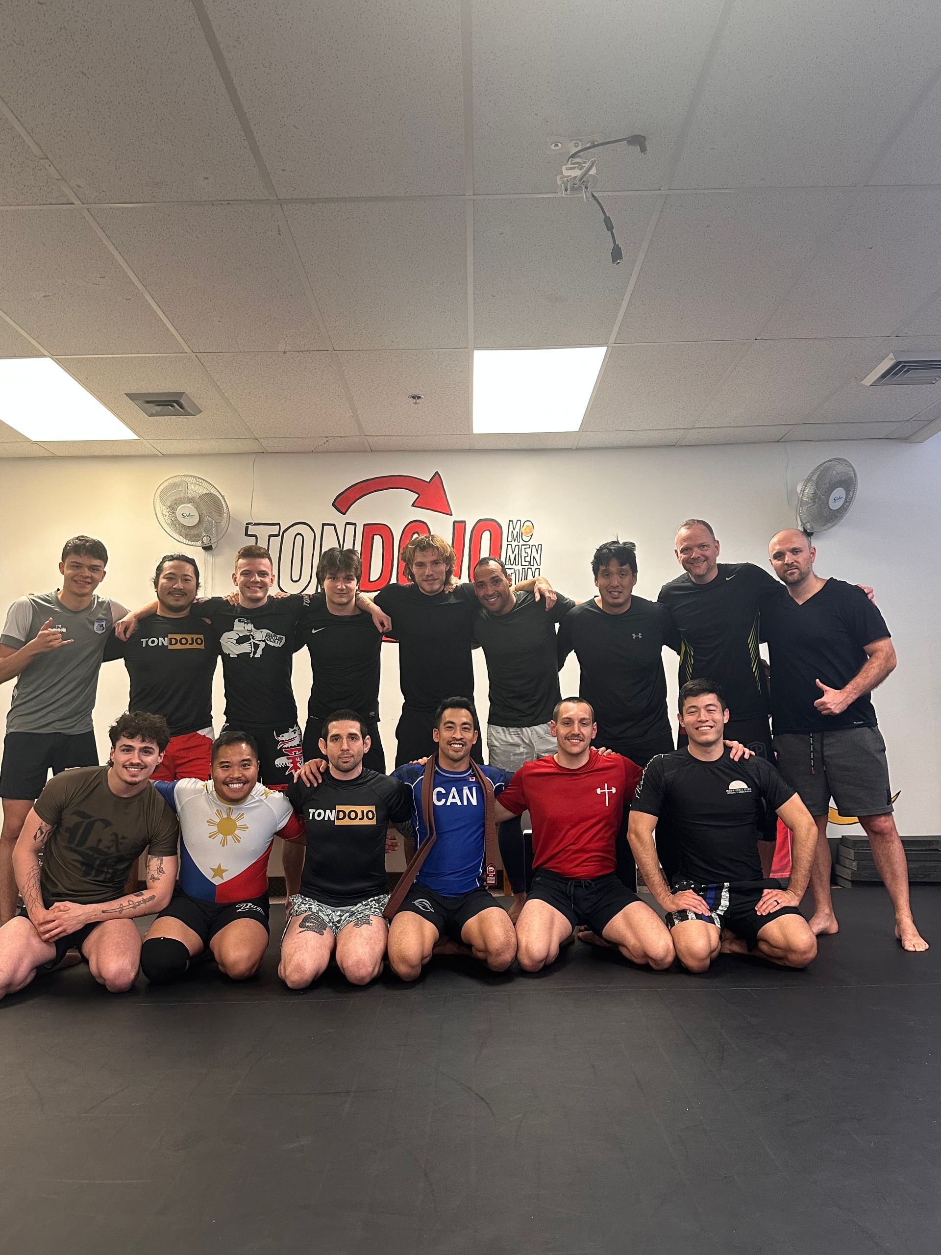 Groupe d'hommes dans une salle de sport, posant pour une photo. La plupart portent des vêtements de sport et sourient.