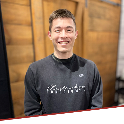 A young man wearing a black sweater with the word masterskye on it is smiling.