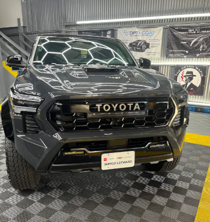 Black Toyota truck parked indoors on a checkered floor, front view with custom grille and off-road tires