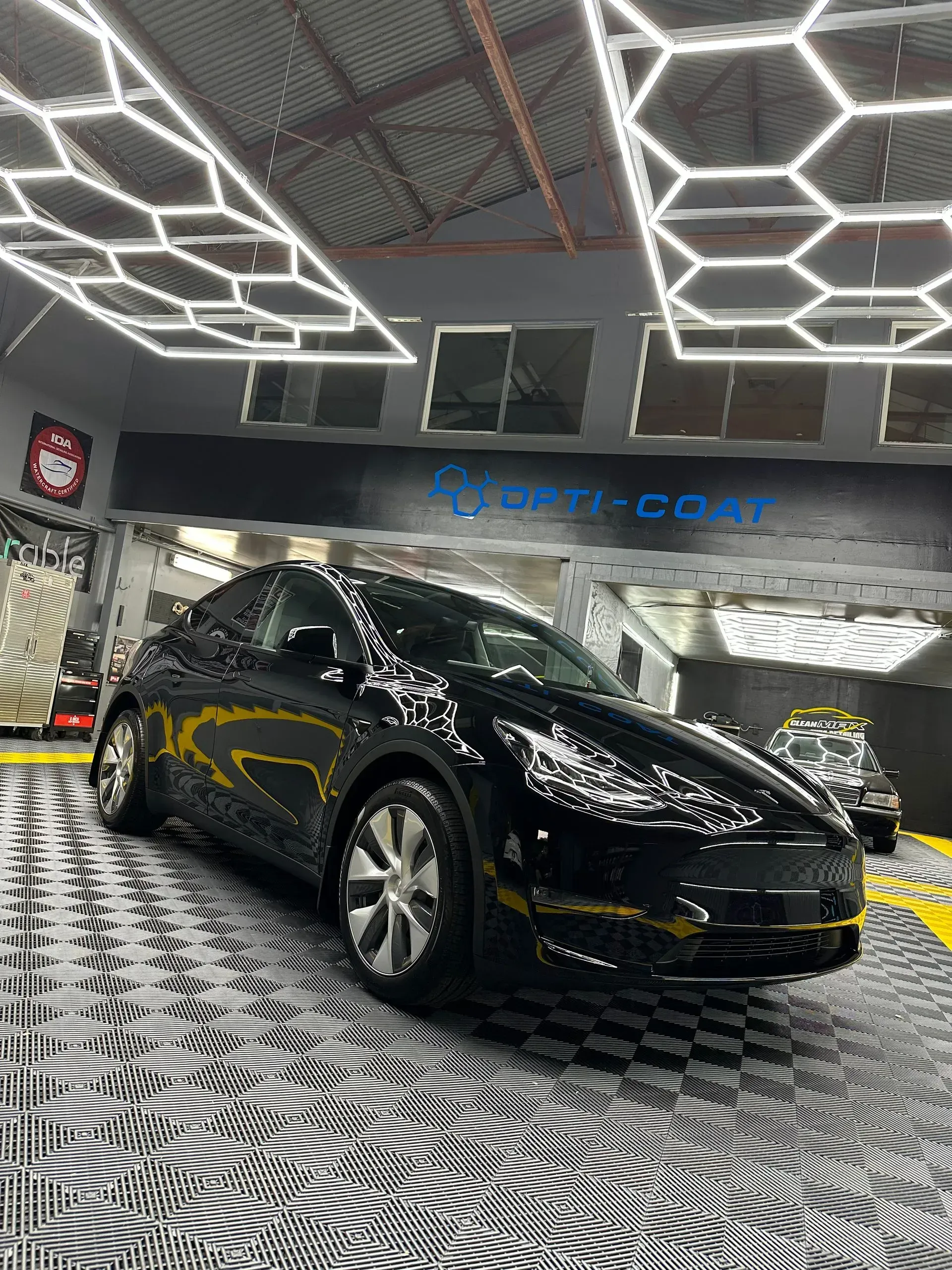 Black Tesla sedan in a showroom with geometric ceiling lights and patterned black-and-white floor