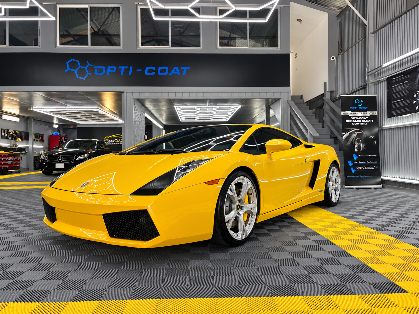 Yellow sports car in a showroom with geometric ceiling lights and an Opti-Coat sign above.