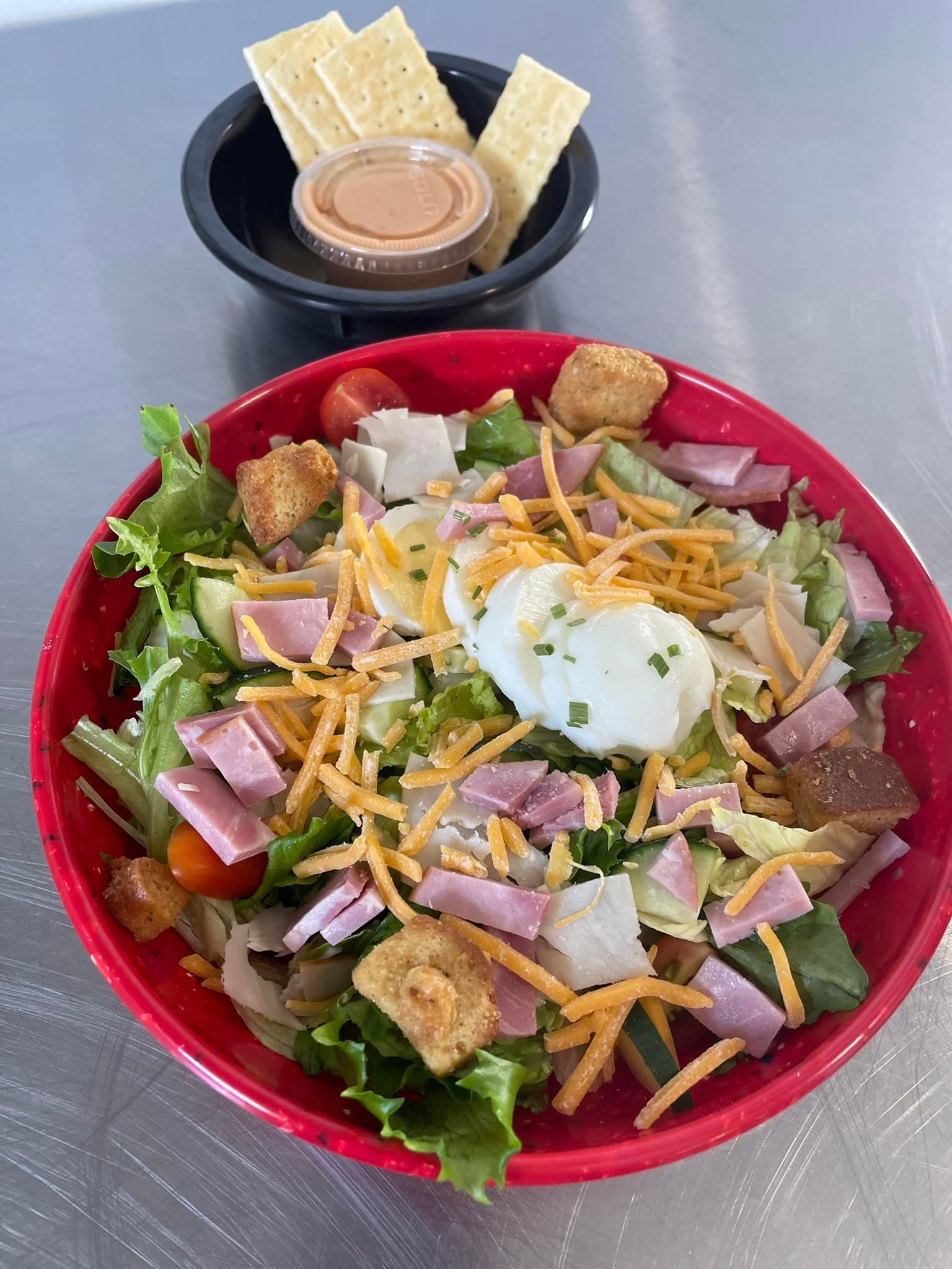 A salad in a red bowl next to a bowl of crackers.