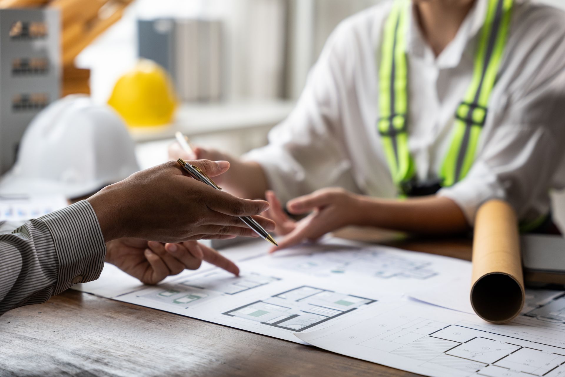 Two professionals discussing architectural blueprints spread on a wooden table.