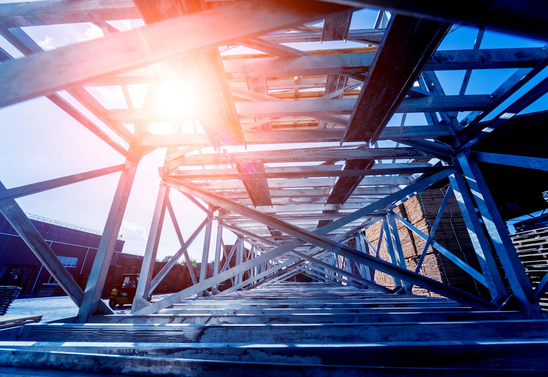 Sunlit steel truss structure with intersecting beams viewed from below.