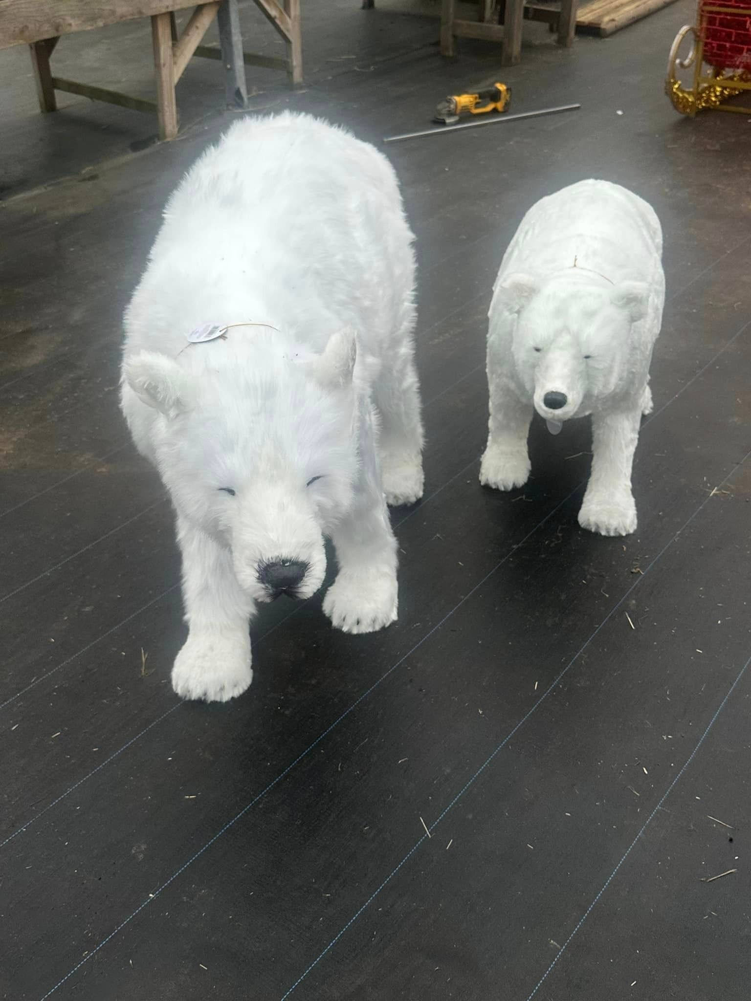 Two white polar bear statues on a dark surface, the larger one in front, both facing forward.