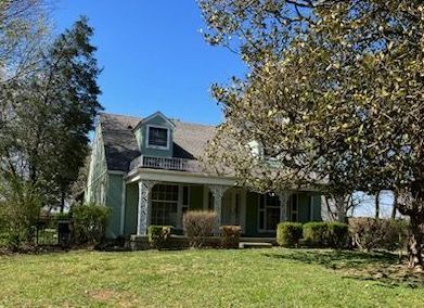 A green house with a porch and trees in front of it.