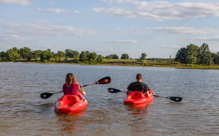 A man and a woman are paddling kayaks on a lake.